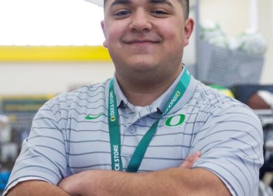 Man standing with arms crossed wearing University of Oregon lanyard.