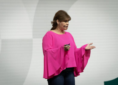Woman in a bright pink top speaking on stage with open hands