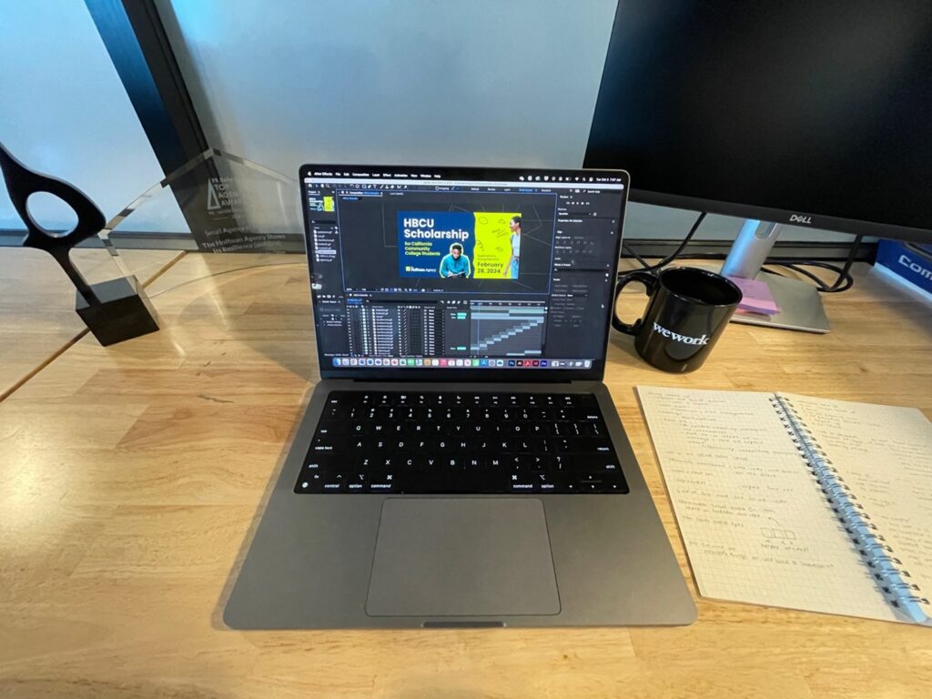 Work laptop sitting on wood desk next to coffee mug and open notebook.