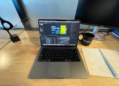 Work laptop sitting on wood desk next to a coffee mug and piece of paper with Adobe Illustrator open.