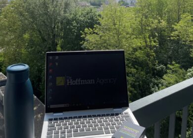 Laptop showing The Hoffman Agency logo sitting on the railing of a scenic nature overlook.