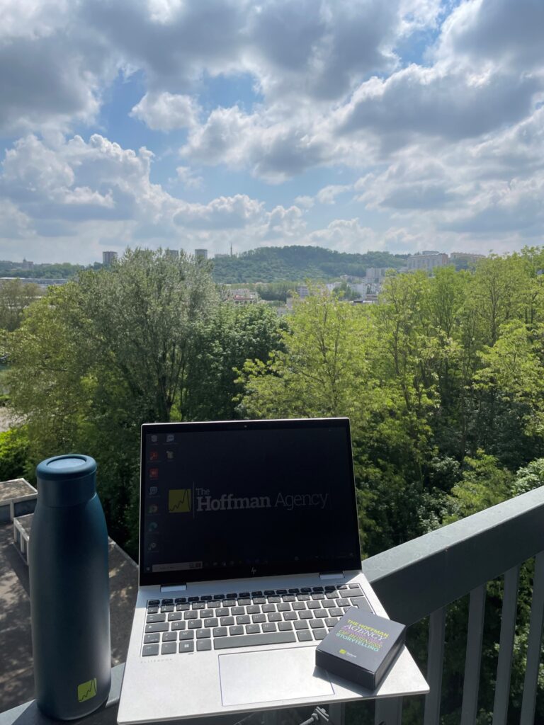 Laptop showing The Hoffman Agency logo sitting on the railing of a scenic nature overlook.