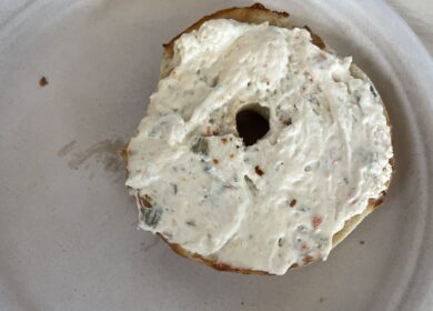 Bagel half, covered in cream cheese, sitting on a styrofoam plate.