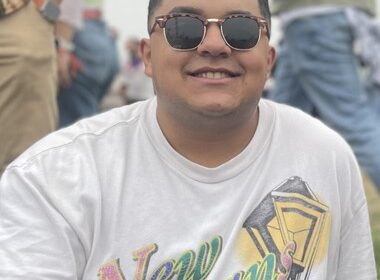 Happy young professional sitting outside in a New Orleans t-shirt and sunglasses.