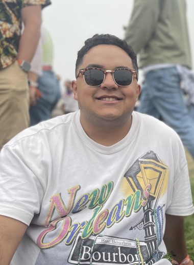 Happy young professional sitting outside in a New Orleans t-shirt and sunglasses.