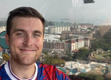 Man in bright blue and red shirt standing in front of cable car and scenic overlook.