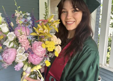 Woman in graduation gown and cap holding a large bouquet of flowers.