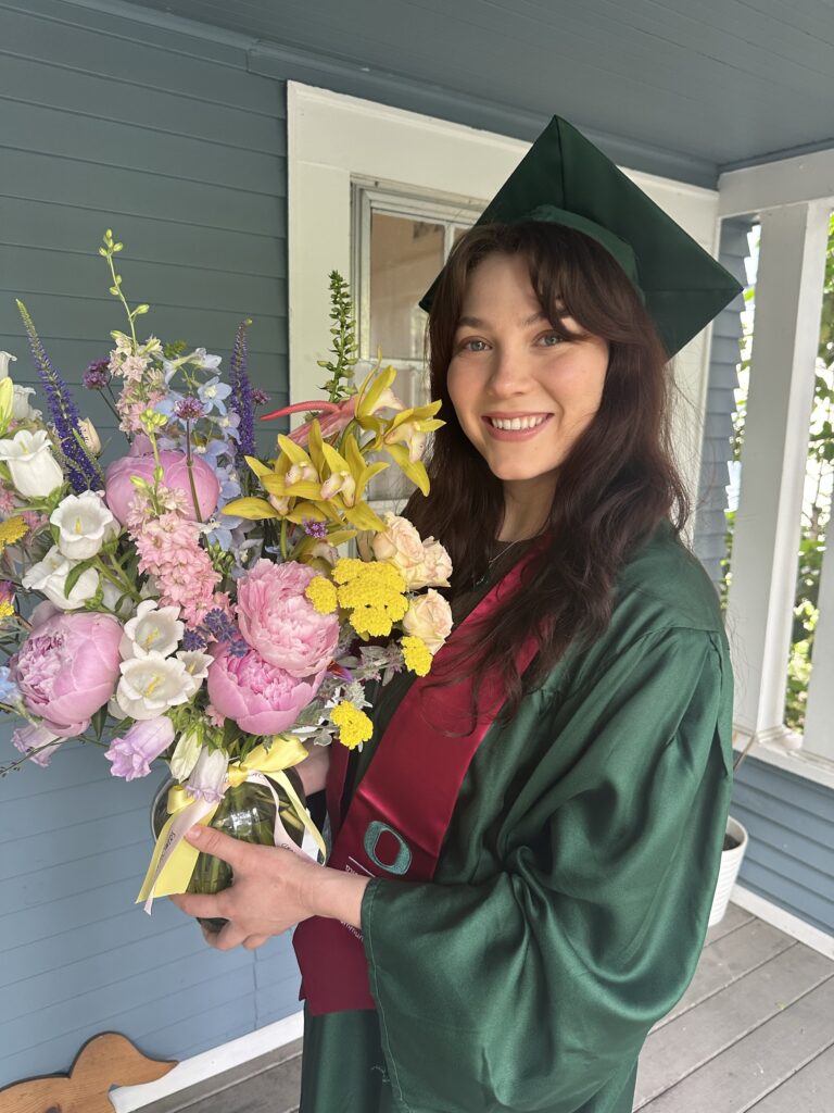 Woman in graduation gown and cap holding a large bouquet of flowers.