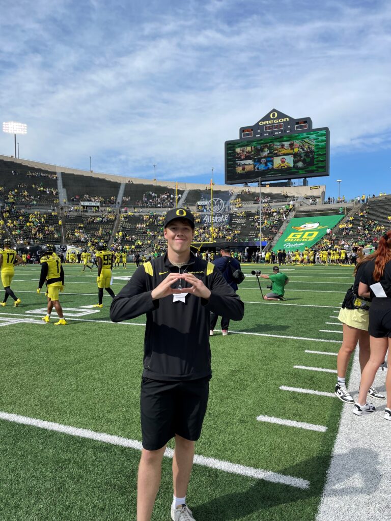 Man standing on football field holding his hands in the shape of an O. 