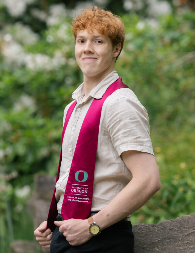 Man standing outdoors in graduation regalia. 