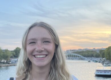 Woman with short blonde hair standing by waterfront sunset.